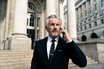Senior businessman talking on smart phone near financial building