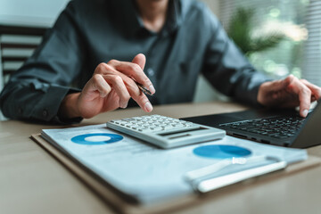 An accountant is seated at a desk in the office, utilizing a calculator to determine balances,...