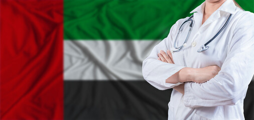 Doctor with crossed arms on United Arab Emirates flag. United Arab Emirates health and care concept. Female doctor on United Arab Emirates flag