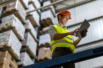 Smiling worker wearing hardhat using tablet PC by railing in warehouse