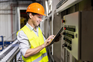 Smiling worker using tablet PC by control panel in warehouse