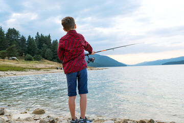 Kid fishing highland lake surrounded pine-covered hills calm water reflection outdoor peaceful day...