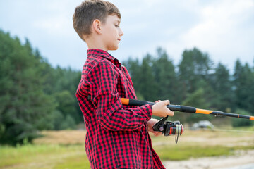 Outdoor childhood activity boy fishing scenic lake view mountains forest background sunny summer...