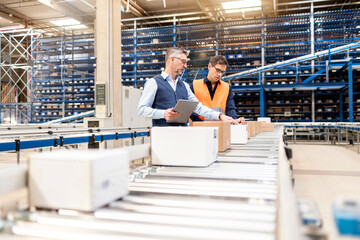 Manager discussing over cardboard boxes with colleague by conveyor belt in warehouse