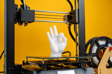Plastic hand model being printed by 3D printer, filament roll placed nearby, vibrant yellow studio background, innovation in progress, concept of rapid prototyping, personalized object creation, DIY 