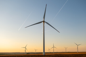 Wind energy infrastructure placed across farmland, high towers equipped rotating blades, converting...
