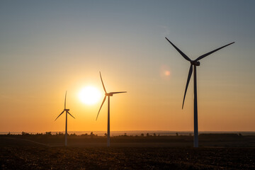 Modern wind generators installed across scenic landscape, harnessing wind energy to create sustainable electricity, eco-friendly solutions to climate issues, rural countryside during golden hour