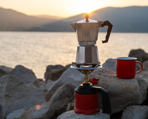Moka espresso maker standing beside red mug, lakeside wood deck scene bathed in sunlight, perfect...