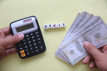 DEBIT Concept with Hand Holding Sign, Calculator, and Rolled Dollar Bills – Economic and Labor...