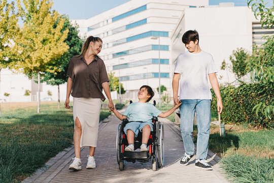 Boy in a wheelchair with his family, mother and brother walking down the street