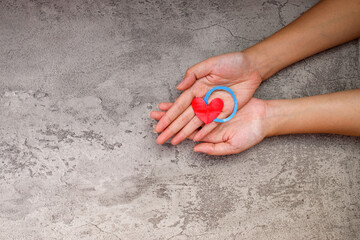 Hands Gently Holding Red Heart And Blue Circle Diabetes Symbol Over Textured Gray Background