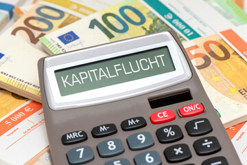 Ein Taschenrechner mit dem Wort Kapitalflucht im Display steht auf vielen Bündel mit Euro Bargeld