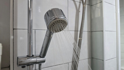 Modern chrome shower head spraying water with shampoo and conditioner bottles nearby, illustrating...