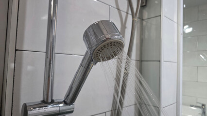 Close-up of chrome shower head spraying water in a tiled bathroom, representing hygiene, plumbing,...