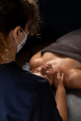 Massage therapist wearing mask providing facial treatment to client in dimly lit spa room