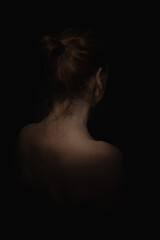 Back view portrait of a woman with tied hair on black background in low lighting