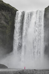 Traveler in Pink Raincoat Facing Majestic Skógafoss Waterfall in Iceland