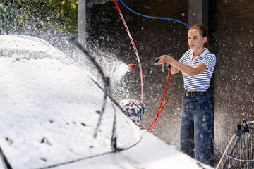 Young woman washing her car with high pressure washer and active foam