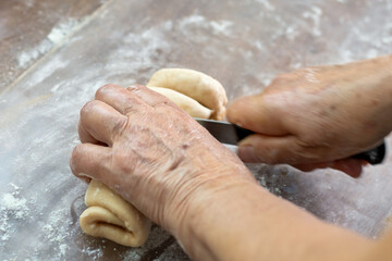 An elderly woman cuts twisted dough for buns. Close-up of her hands