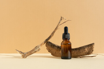Bottle of dark amber glass with hyaluronic acid or face serum near dry branch on a beige background. Concept natural cosmetics with organic components. Copy space for your design. Front view.