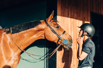Horse rider wearing helmet adjusting chin strap while looking at horse