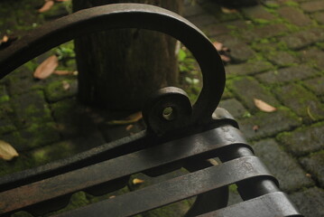 An old rusty metal bench sits in a park under a green tree near a well