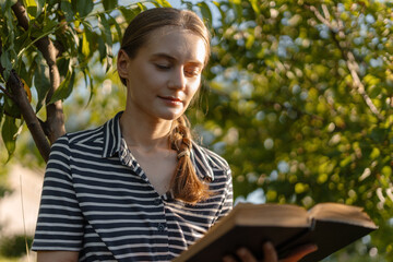 Young woman reading a book in the garden enjoying the summer sunlight