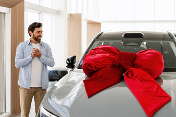 Happy customer admiring his new car with big red bow in dealership