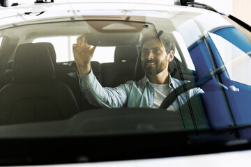 Handsome man adjusting rearview mirror while sitting in new car