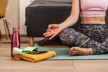  Woman meditating in lotus position at home with bottle and towel on yoga mat © Juan Algar