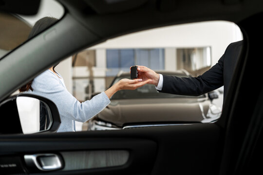 Salesman giving car keys to customer in dealership showroom