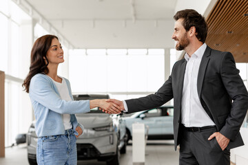 Salesman shaking hands with customer buying new electric car in dealership