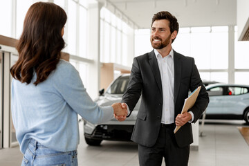 Car salesman shaking hands with customer in dealership showroom
