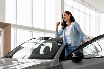 Excited woman celebrating buying new car in dealership showroom