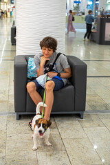 boy resting in a chair in a shopping center with a jack russell terrier on the pavement
