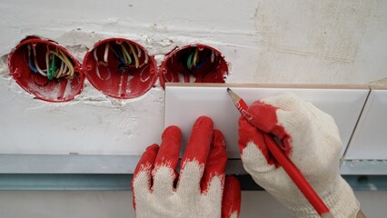 Construction worker marking a white ceramic tile near three electric sockets with red caps and some wires