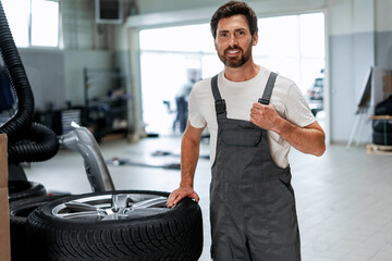 Mechanic showing thumbs up while holding car tire in auto repair shop