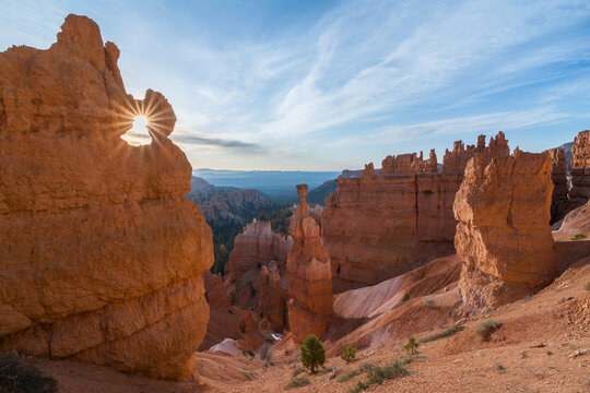 The sun shines through a hole in a rock formation in Bryce Canyon National Park, Utah, illuminating the landscape with its golden rays. - Powered by Adobe