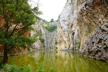 view in the valley with the orange-colored rocky mountains, cliffs and a pond in the middle of the valley. The reflection of the water can see the cliffs in the middle of the forest.