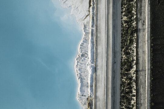 Aerial view of turquoise water meeting the chalky white shore beside the dark land, creating a stark contrast of color and texture, Nancy, Grand Est, France.