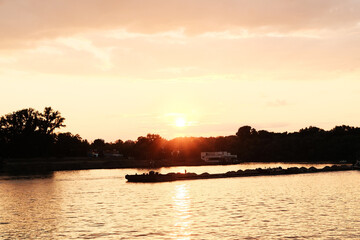 Serene sunset over the Sava River in Belgrade, Serbia, with warm orange tones and a passing barge...