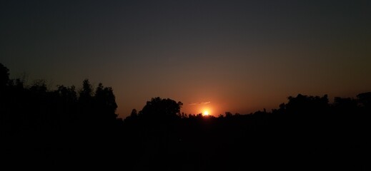 Naklejka premium Sunset glowing over mountain landscape with colorful sky and silhouetted trees