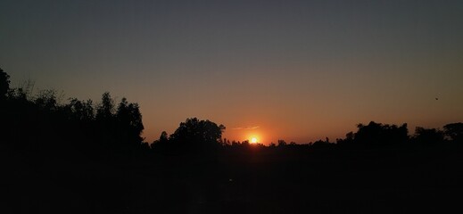 Fototapeta premium Beautiful golden sunset light silhouettes mountains and cityscapes under an orange evening sky with scattered clouds