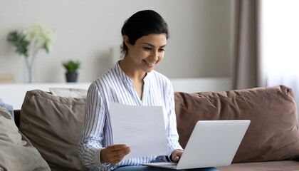 _Young indian woman holding letter using laptop computer application paying bill onlin .