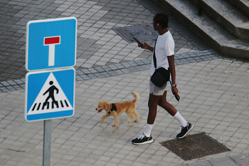 Hombre negro paseando a su perro por la calle mientras mira su teléfono móvil junto a señales de...
