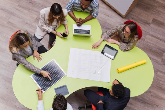 High angle view of business colleagues having a meeting with plan, wireless devices and solar panel on table