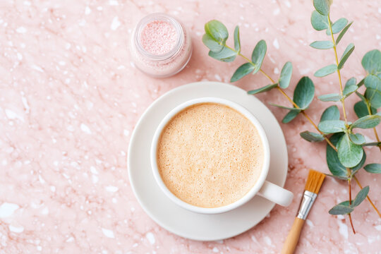 White ceramic cup with latte on plate alongside brush and jar overhead minimalist composition