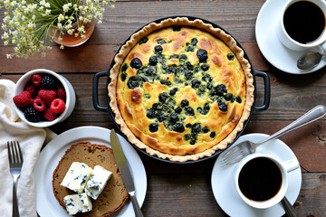 Homemade blueberry quiche in cast iron skillet with fresh berries and coffee cups on wooden table, rustic brunch setting perfect for weekend entertaining