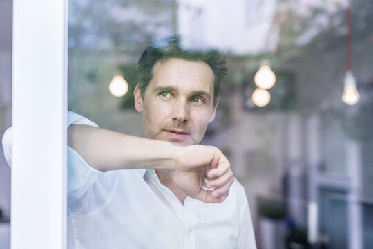 Thoughtful handsome mature businessman looking out through office window