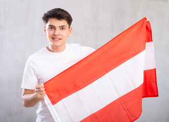 Reliant positive young man holds big national flag of Austria with confident smile showing teeth....